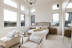 Bedroom with a high ceiling, light colored carpet, and a notable chandelier