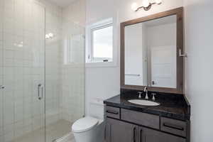 Bathroom featuring an enclosed shower, toilet, and vanity