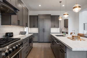 Kitchen featuring built in appliances, dark hardwood / wood-style flooring, sink, an island with sink, and custom range hood