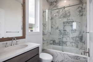 Full bathroom featuring vanity, toilet, and bath / shower combo with glass door