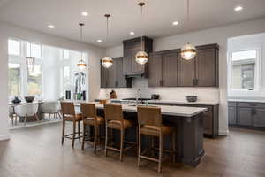 Kitchen featuring tasteful backsplash, a kitchen breakfast bar, wood-type flooring, hanging light fixtures, and a center island with sink