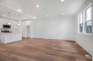 Kitchen featuring white cabinets, light hardwood / wood-style floors, pendant lighting, a center island with sink, and range