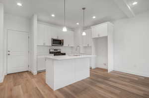 Kitchen featuring light hardwood / wood-style flooring, stainless steel appliances, white cabinets, and a kitchen island with sink