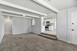 Unfurnished living room with beamed ceiling and light colored carpet