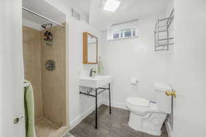 Bathroom featuring toilet, tiled shower, and sink