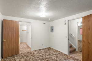 Carpeted spare room featuring a textured ceiling and electric panel