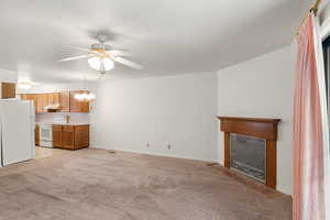 Unfurnished living room featuring ceiling fan with notable chandelier, light carpet, and a textured ceiling