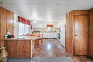 Kitchen featuring white cabinets, white appliances, a chandelier, kitchen peninsula, and pendant lighting