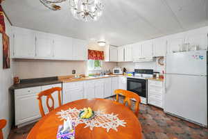 Kitchen with a notable chandelier, sink, white appliances, and white cabinets