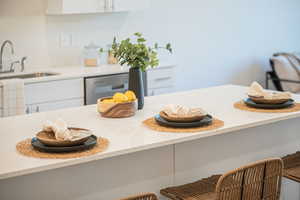 Kitchen with dishwasher, white cabinets, light stone countertops, and sink