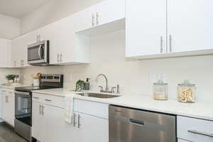 Kitchen featuring stainless steel appliances, dark hardwood / wood-style floors, light stone countertops, white cabinets, and sink