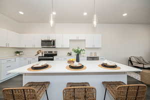 Kitchen featuring a kitchen bar, white cabinets, appliances with stainless steel finishes, and a kitchen island