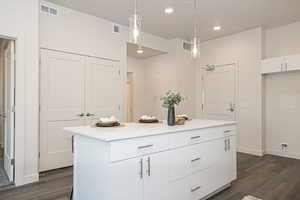 Kitchen featuring decorative light fixtures, dark wood-type flooring, white cabinetry, and a center island