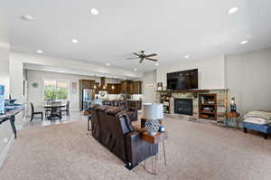 Carpeted living room featuring ceiling fan and a stone fireplace