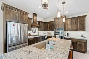 Kitchen featuring appliances with stainless steel finishes, custom range hood, light stone counters, and sink