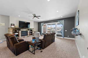 Carpeted living room featuring ceiling fan and a stone fireplace