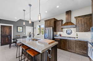 Kitchen with sink, appliances with stainless steel finishes, custom range hood, a center island with sink, and light tile patterned flooring