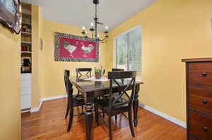 Dining space with hardwood flooring, large window providing natural light, and a notable chandelier