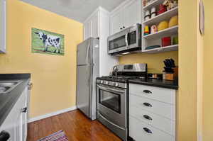 Kitchen featuring appliances with stainless steel finishes, dark hardwood  flooring, and white cabinetry