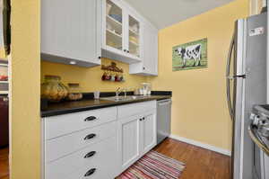 Kitchen with dark hardwood  flooring, appliances with stainless steel finishes, white cabinetry, and sink