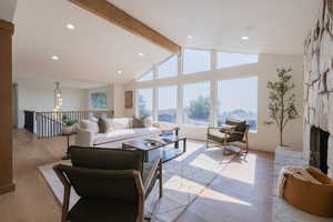 Living room featuring a fireplace, light wood-type flooring, high vaulted ceiling, and beam ceiling