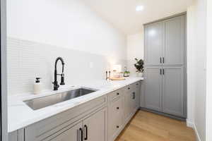 Kitchen with gray cabinetry, light hardwood / wood-style flooring, light stone counters, sink, and tasteful backsplash