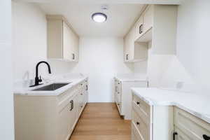 Kitchen featuring sink, light stone countertops, white cabinetry, and light hardwood / wood-style floors