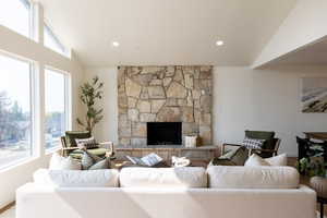 Living room featuring vaulted ceiling, wood-type flooring, and a stone fireplace