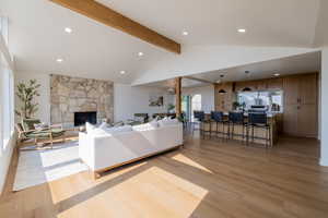 Living room with high vaulted ceiling, beamed ceiling, a stone fireplace, and wood-type flooring