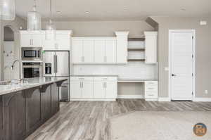 Kitchen with hanging light fixtures, light hardwood / wood-style flooring, white cabinetry, appliances with stainless steel finishes, and light stone countertops