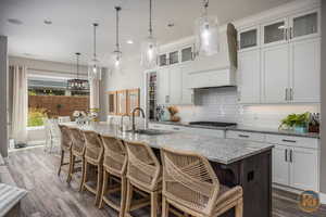 Kitchen with hanging light fixtures, white cabinetry, stainless steel gas cooktop, a center island with sink, and sink