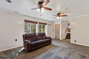 Carpeted living room with crown molding and ceiling fan, door to the outside patio.