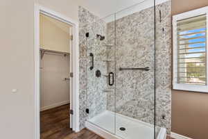 Bathroom featuring a shower with full glass door, a healthy amount of sunlight, and hardwood / wood-style floors. walk in closet