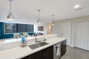 Kitchen featuring dark brown cabinetry, sink, hanging light fixtures, stainless steel dishwasher, and light hardwood / wood-style floors