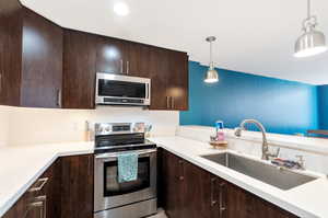 Kitchen featuring hanging light fixtures, stainless steel appliances, sink, dark brown cabinets, and tasteful backsplash