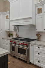 Kitchen with range with two ovens, light stone counters, dark hardwood / wood-style flooring, and white cabinetry