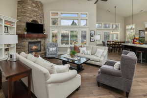 Living room featuring a fireplace, high vaulted ceiling, wood-type flooring, and ceiling fan