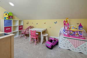 Rec room with lofted ceiling, light colored carpet, and a textured ceiling