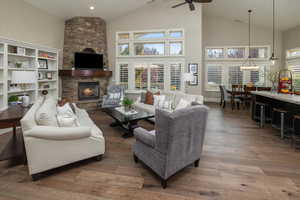 Living room featuring dark hardwood / wood-style floors, high vaulted ceiling, ceiling fan, and a stone fireplace