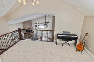 Sitting room featuring a textured ceiling, vaulted ceiling, ceiling fan with notable chandelier, and a stone fireplace