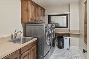 Laundry area featuring light tile patterned floors, sink, cabinets, and washer and dryer