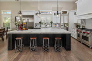 Kitchen with high end appliances, white cabinetry, a kitchen bar, wood-type flooring, and decorative backsplash