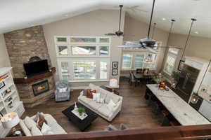 Living room with high vaulted ceiling, ceiling fan, dark hardwood / wood-style flooring, and a stone fireplace