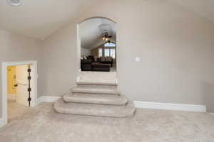 Staircase featuring lofted ceiling, ceiling fan, and carpet