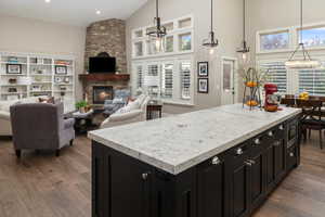 Kitchen featuring high vaulted ceiling, wood-type flooring, a kitchen island, and a stone fireplace