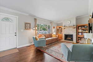 Living room featuring dark wood-type flooring, ornamental molding, and a stone fireplace