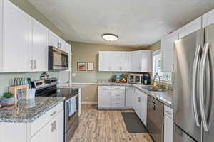 Kitchen with a textured ceiling, light hardwood / wood-style flooring, appliances with stainless steel finishes, sink, and white cabinets