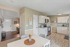 Kitchen with appliances with stainless steel finishes, light hardwood / wood-style flooring, and white cabinets