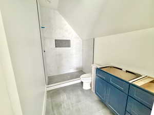 Bathroom with vaulted ceiling, tiled shower, and toilet