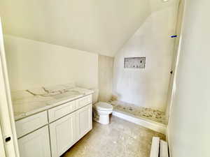 Bathroom with vanity, toilet, vaulted ceiling, and a tile shower